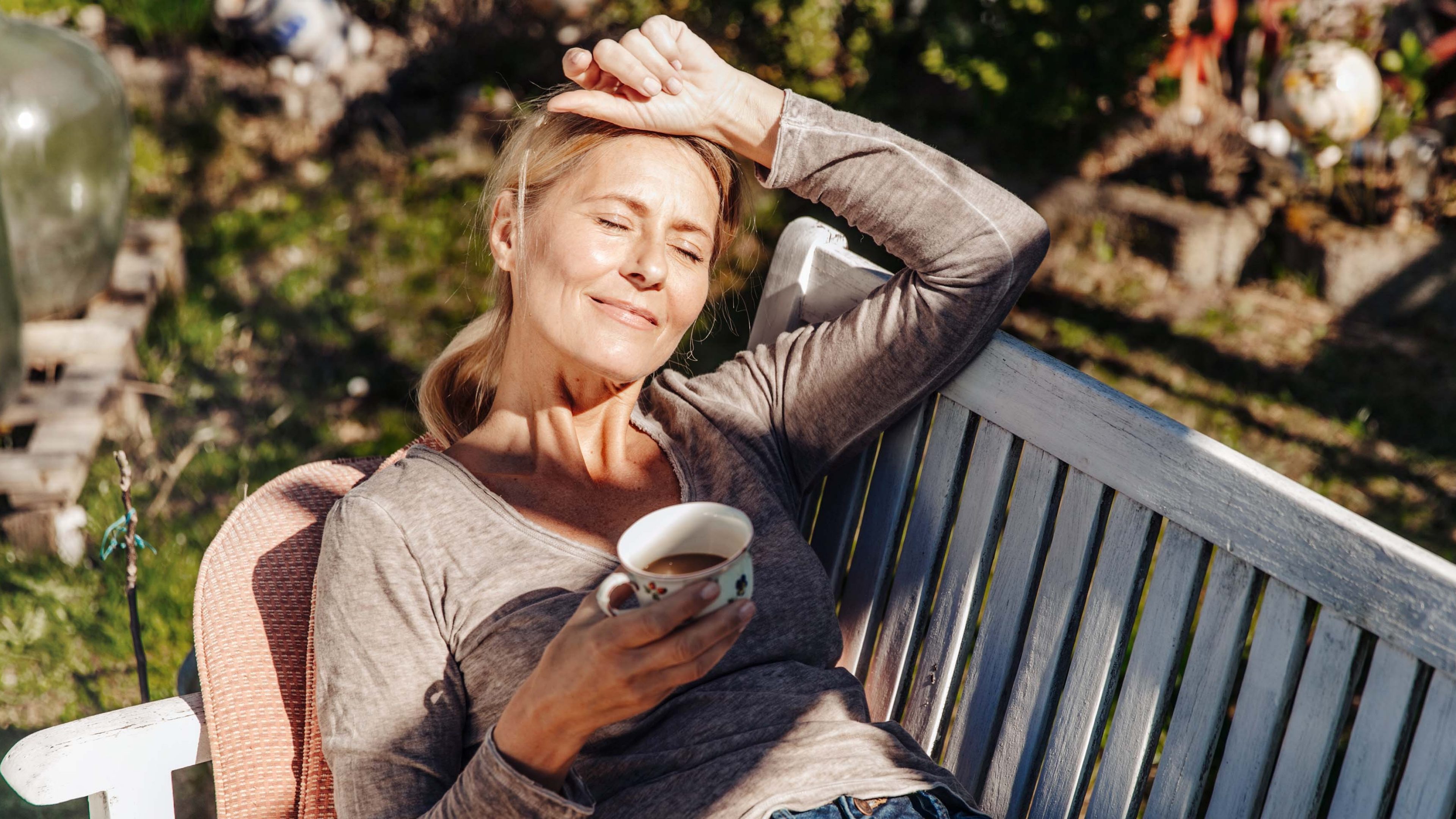 Frau sitzt auf einer Bank mit einem Kaffee in der Hand und denk über eine Frühpensionierung nach