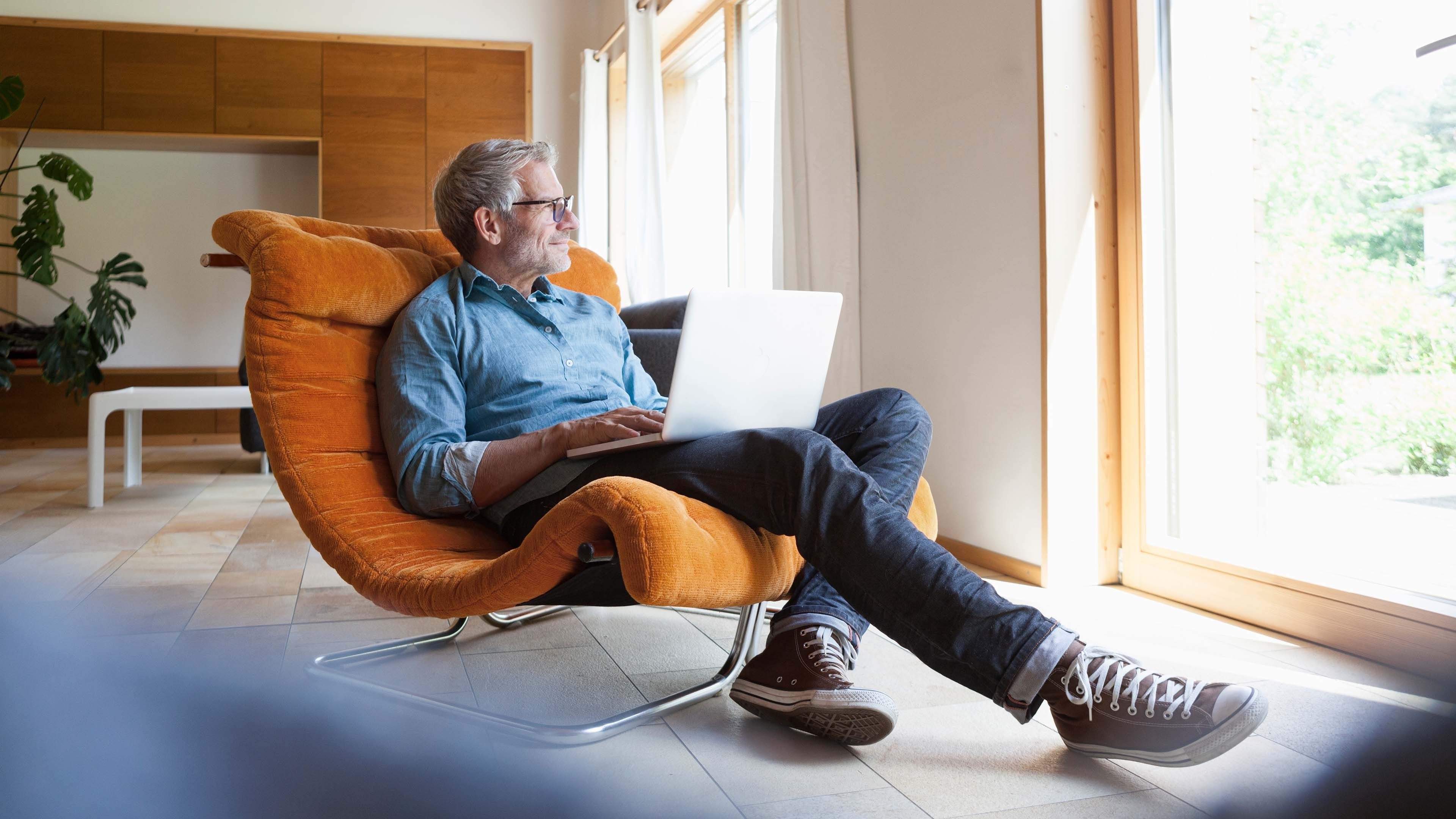 Mann sitzt im Sessel mit Laptop auf der Schoss und macht sich Gedanken über sein Vermögen