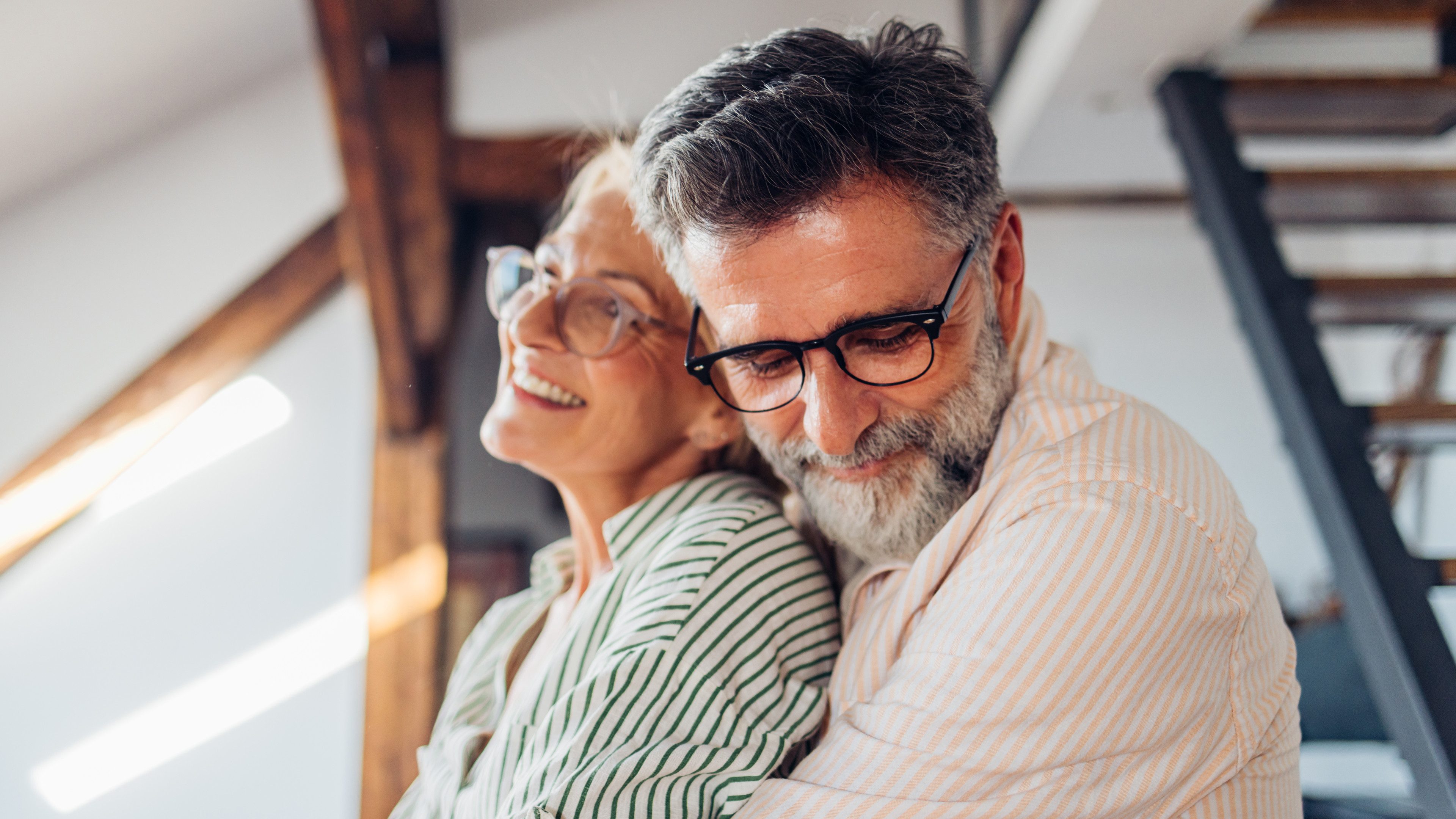 Close-up of a joyful elderly couple embracing in a cozy home setting. They are smiling and enjoying a tender moment together.