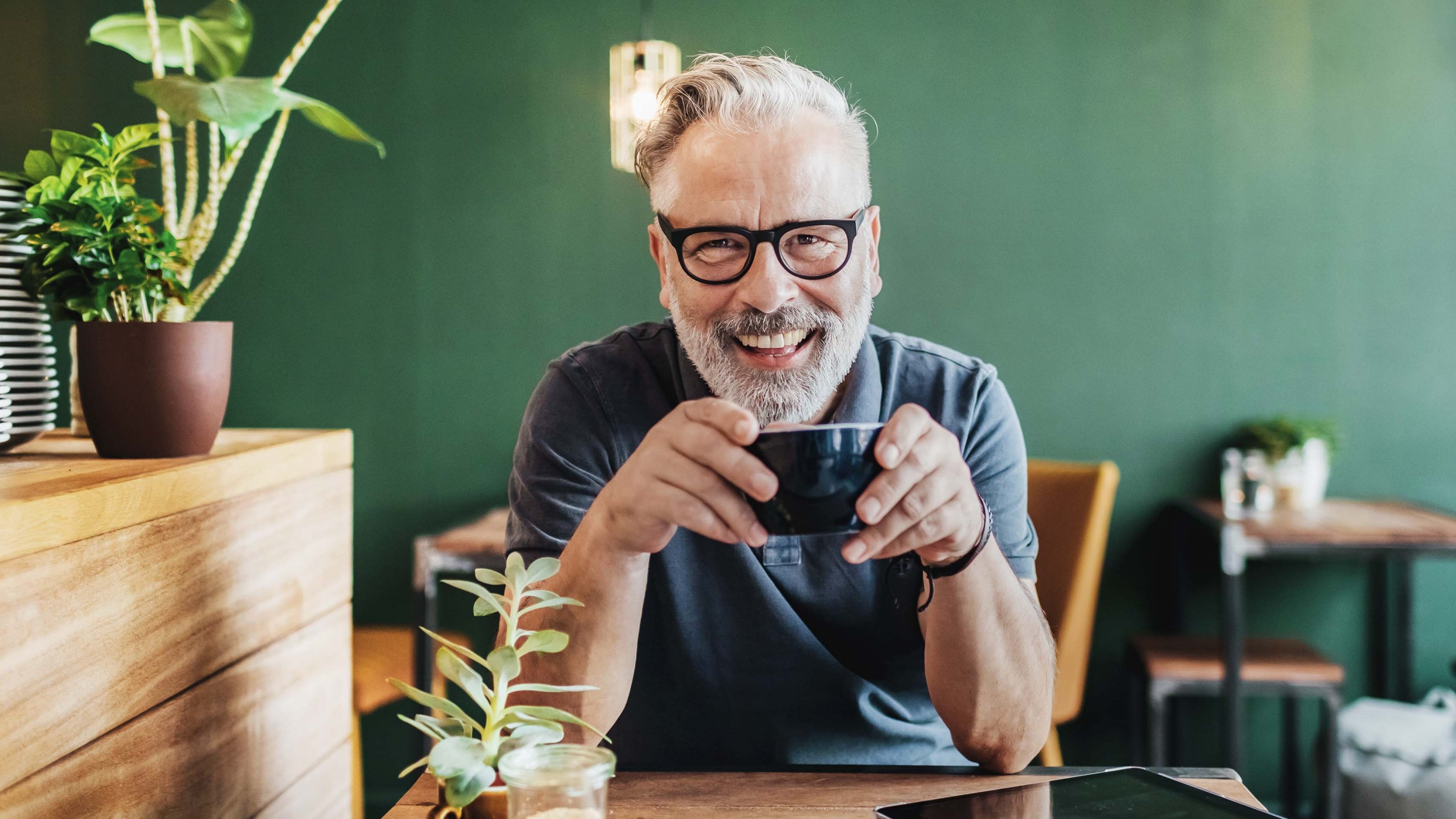 Mann sitzt im Kaffee mit einer Kaffeetasse in der Hand und freut sich auf die Pensionierung