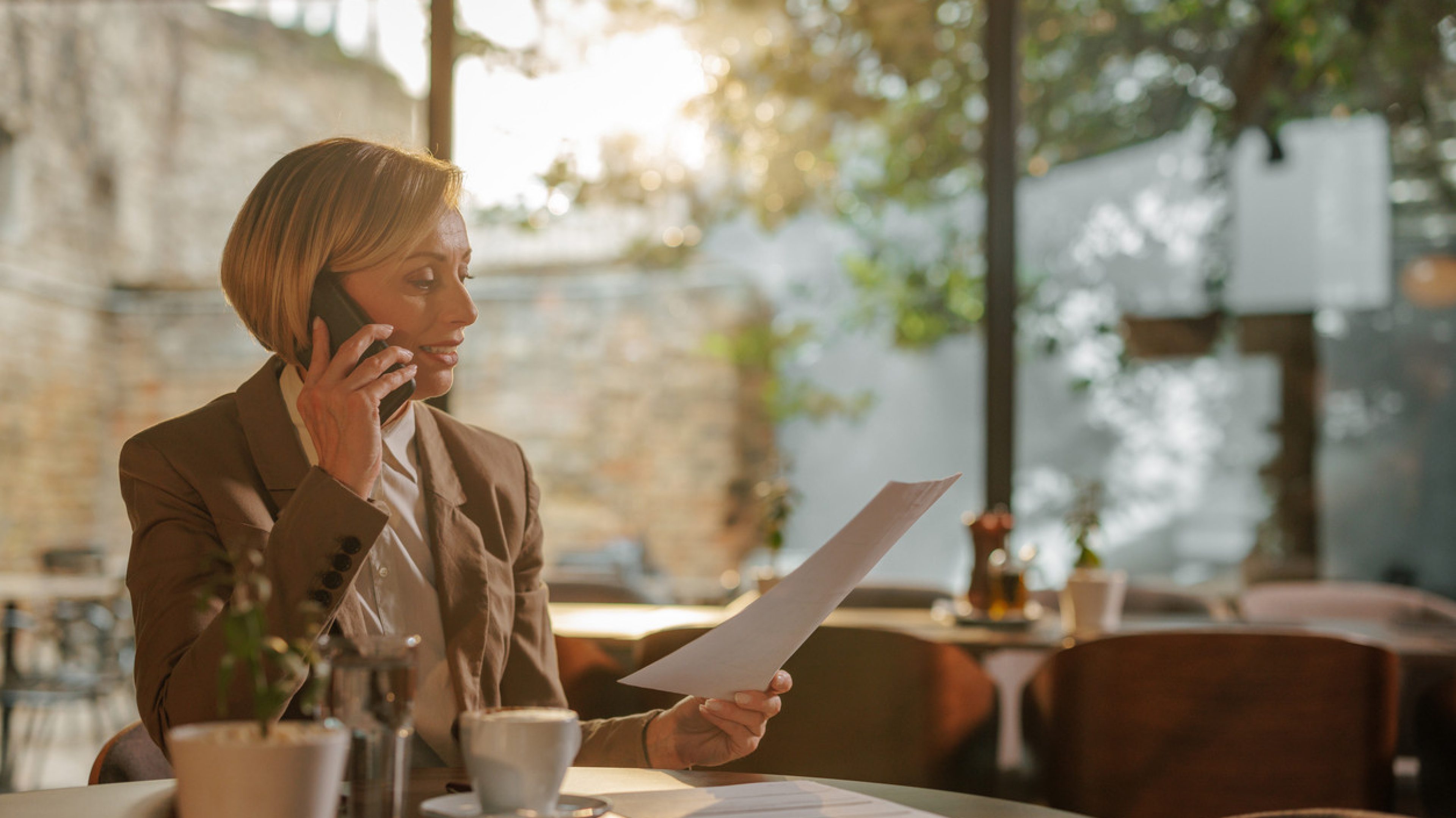Frau sitzt im Cafe und studiert eine Information zum Freizügigkeitsgesetz, während sie am Handy telefoniert.