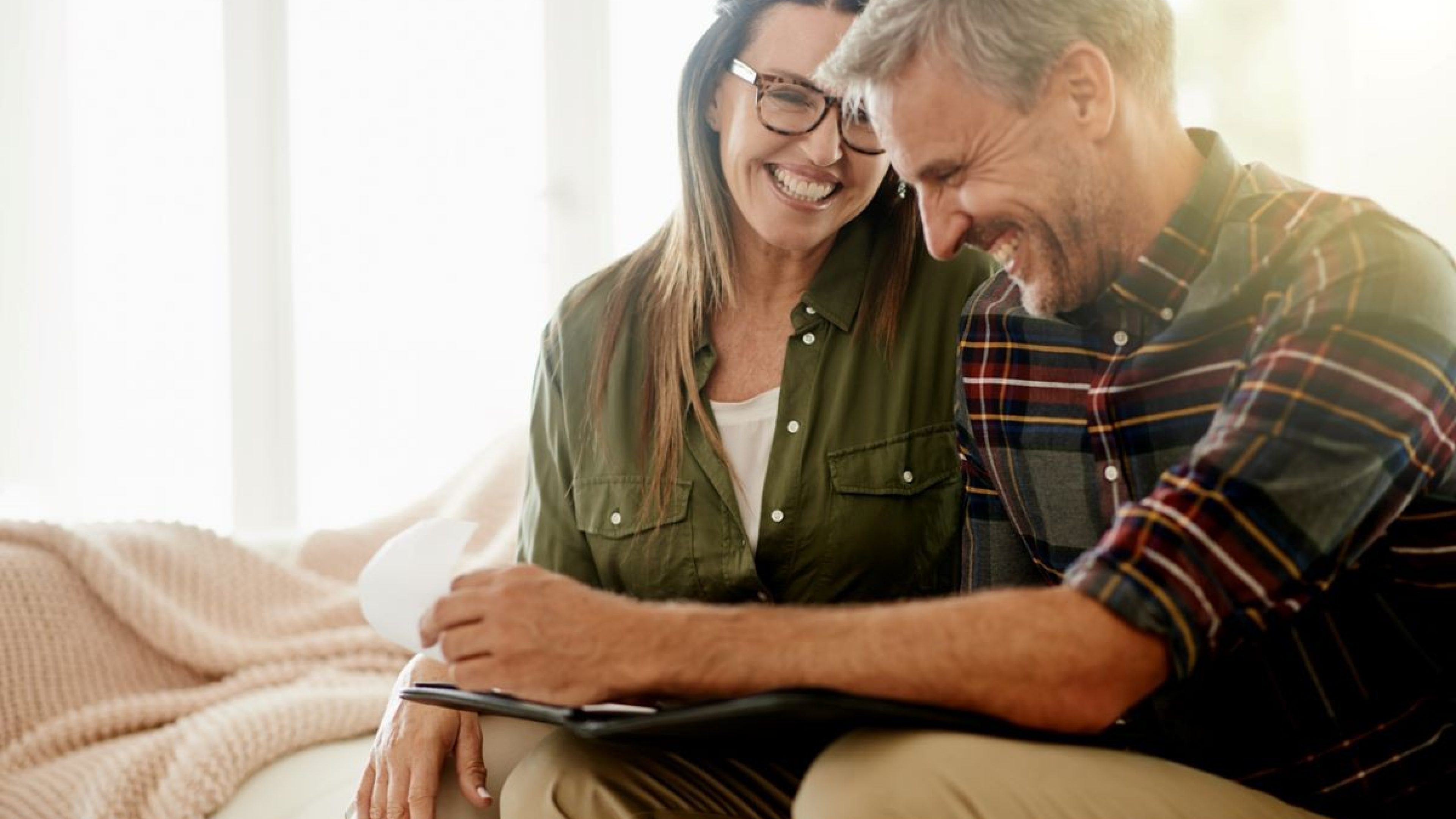 Ein Ehepaar sitzt zufrieden auf dem Sofa. Auf einem Tablet schauen sie sich ihre individuelle Hypothekenstrategie an. 