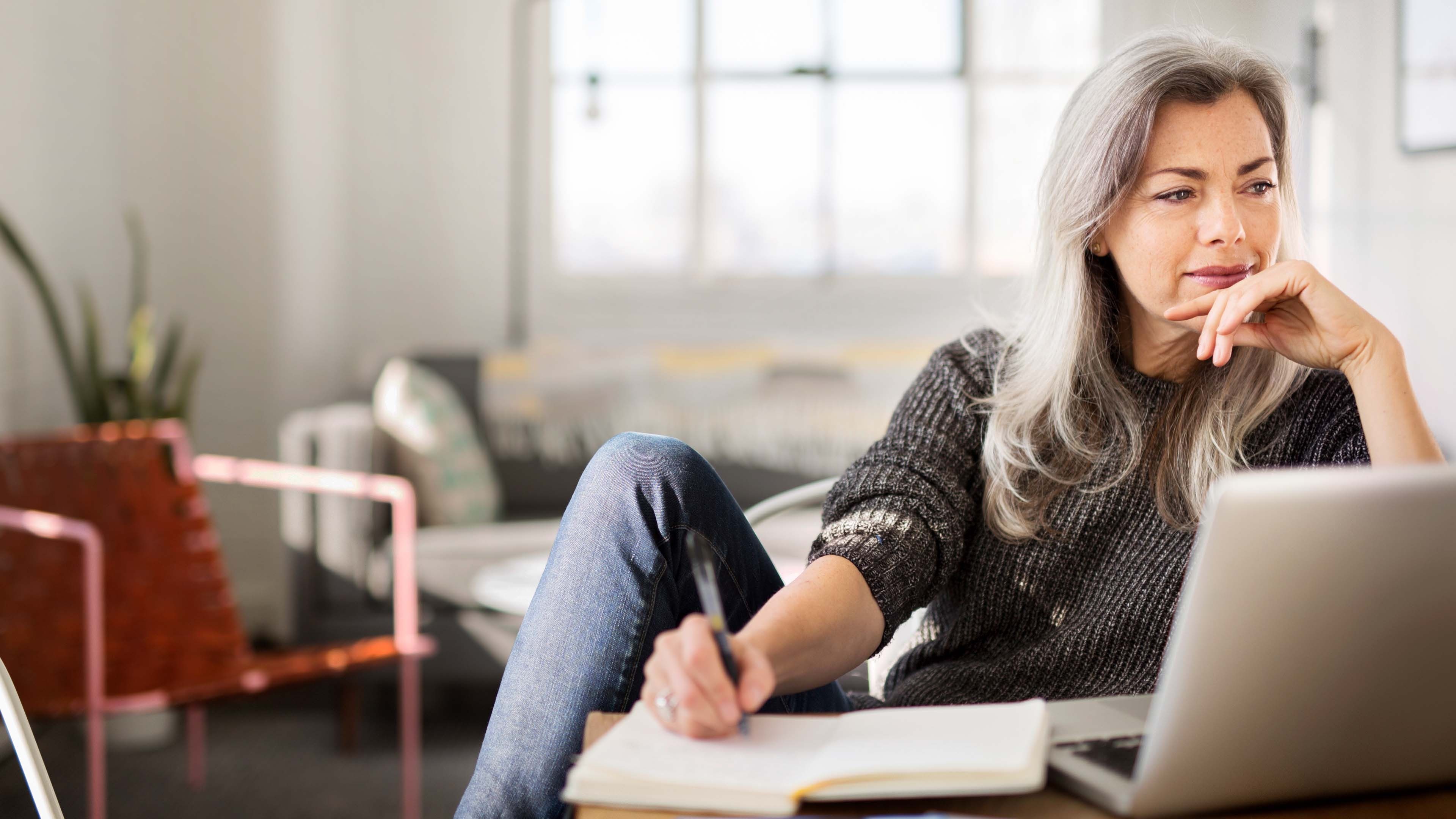 Frau mit grauen langen  Haaren sitzt am Laptop und informiert sich darüber, wie sie ihre Vorsorgelücke schliessen kann