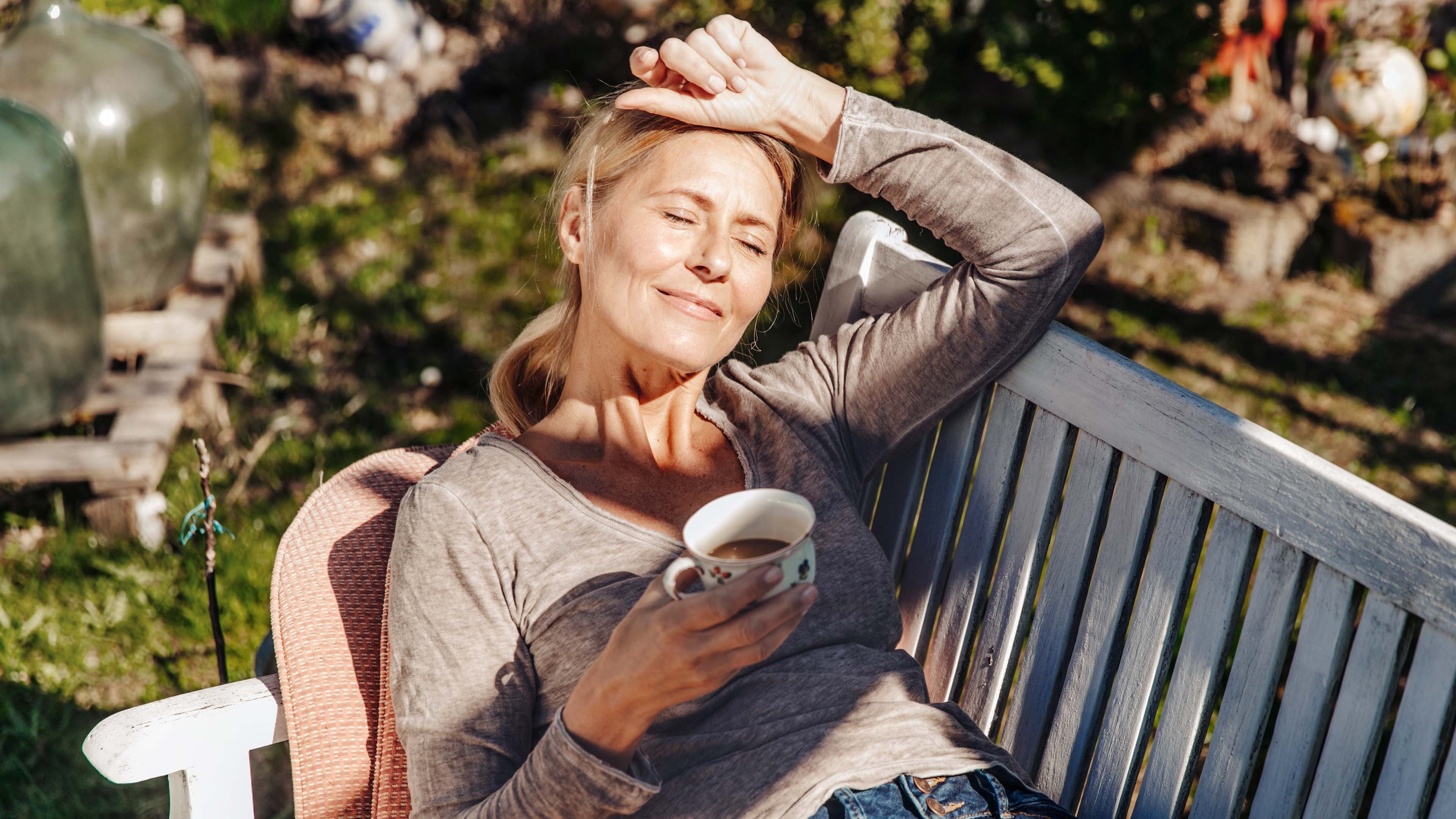 Frau liegt auf einer Bank mit einem Tee in der Hand und freut sich auf ihre Frühpensionierung